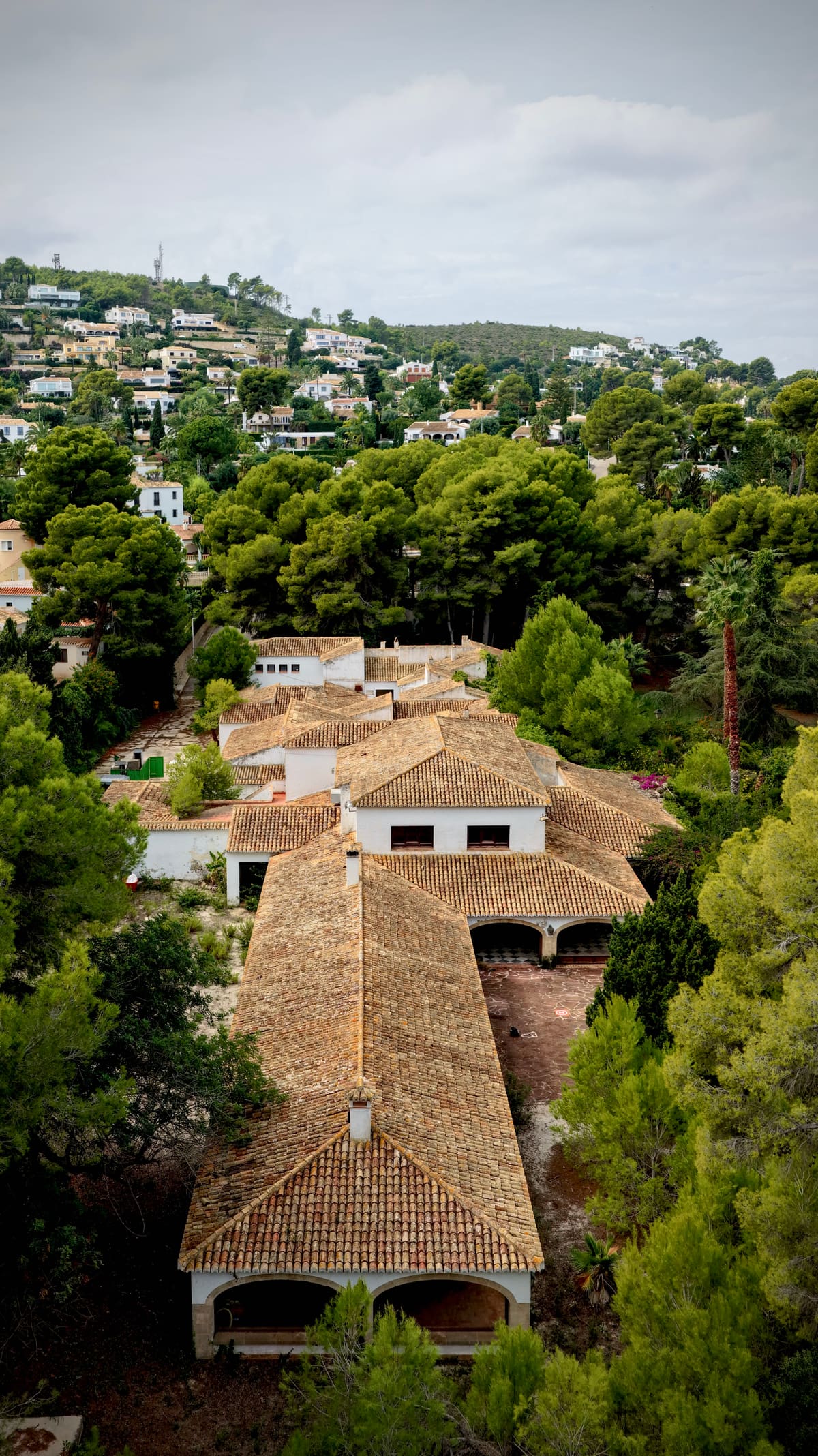 Casa Tosalet — tiled roofs and arched porches among pines, with the hillside of Jávea behind